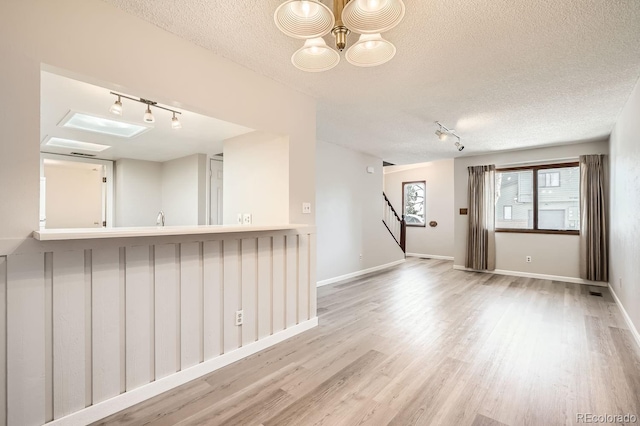 unfurnished room with track lighting, a textured ceiling, a chandelier, and light hardwood / wood-style flooring