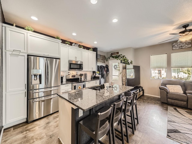 kitchen featuring dark stone counters, an island with sink, white cabinetry, a kitchen breakfast bar, and stainless steel appliances