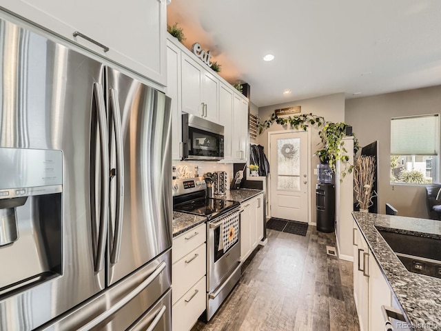 kitchen with dark stone countertops, dark hardwood / wood-style floors, stainless steel appliances, and white cabinets