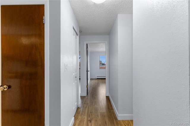 corridor with a baseboard heating unit, baseboards, light wood-style floors, a textured wall, and a textured ceiling