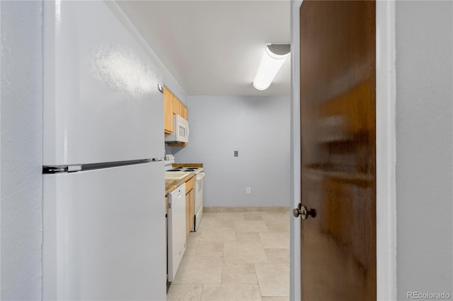 kitchen featuring light brown cabinets, white appliances, light countertops, and baseboards