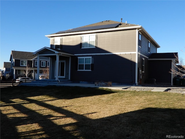 rear view of property featuring a yard and solar panels