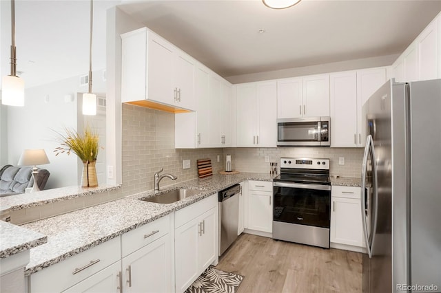 kitchen featuring appliances with stainless steel finishes, light hardwood / wood-style floors, white cabinetry, pendant lighting, and sink