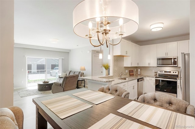 kitchen with light stone counters, a chandelier, sink, stainless steel appliances, and decorative light fixtures