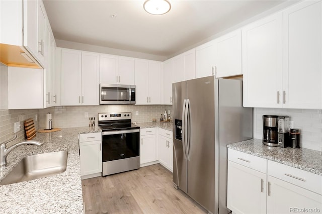 kitchen featuring light hardwood / wood-style floors, white cabinetry, light stone counters, stainless steel appliances, and sink