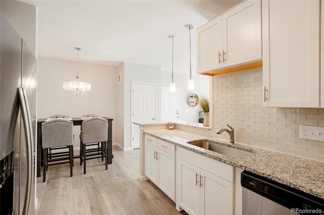 kitchen with light stone counters, pendant lighting, white cabinetry, stainless steel appliances, and light wood-type flooring