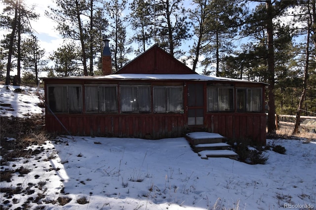 snow covered property featuring a sunroom and a chimney