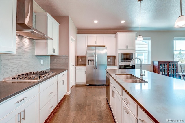 15619 Syracuse Way, Thornton, CO 80602 - kitchen with appliances with stainless steel finishes, wall chimney exhaust hood, wood finished floors, hanging light fixtures, and recessed lighting