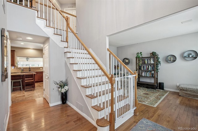 staircase with a towering ceiling, baseboards, visible vents, and hardwood / wood-style floors