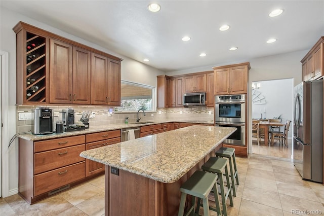 kitchen with a sink, a center island, appliances with stainless steel finishes, light stone countertops, and a kitchen bar