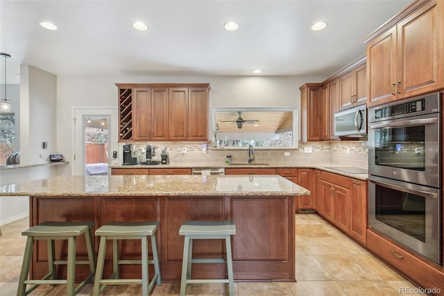 kitchen with brown cabinetry, appliances with stainless steel finishes, decorative light fixtures, a center island, and a sink