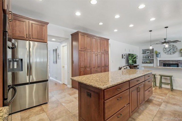 kitchen featuring a center island, brown cabinets, hanging light fixtures, open floor plan, and stainless steel fridge