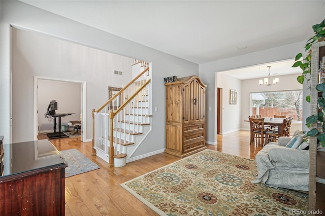 foyer featuring light wood finished floors, baseboards, visible vents, an inviting chandelier, and stairs