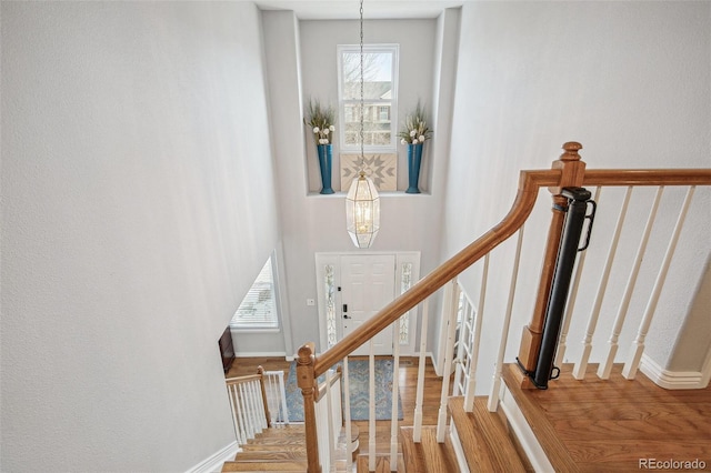 staircase with a notable chandelier, wood finished floors, and baseboards