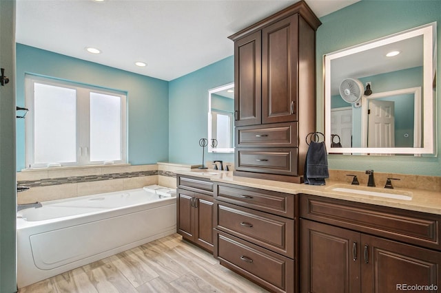 bathroom with wood finished floors, a garden tub, a sink, and double vanity