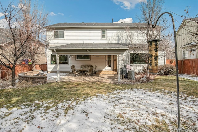 snow covered rear of property with an outdoor fire pit, a patio area, a fenced backyard, and a yard