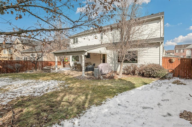 snow covered house featuring a yard, a fenced backyard, and a patio