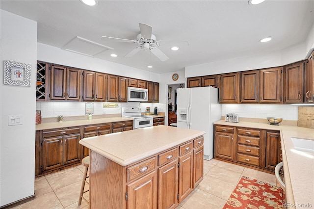 kitchen featuring light tile patterned floors, white appliances, a kitchen breakfast bar, tasteful backsplash, and a kitchen island