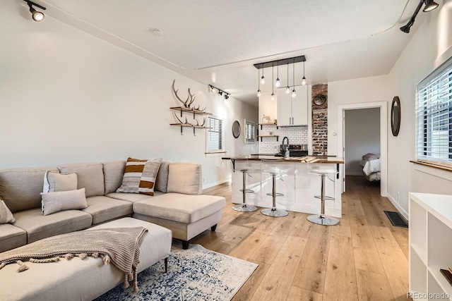 living area featuring light wood-style floors, baseboards, visible vents, and rail lighting