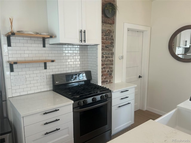 kitchen with open shelves, decorative backsplash, white cabinets, stainless steel range with gas stovetop, and light stone countertops