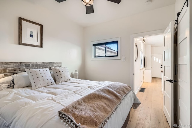 bedroom featuring visible vents, ceiling fan, light wood finished floors, and a barn door