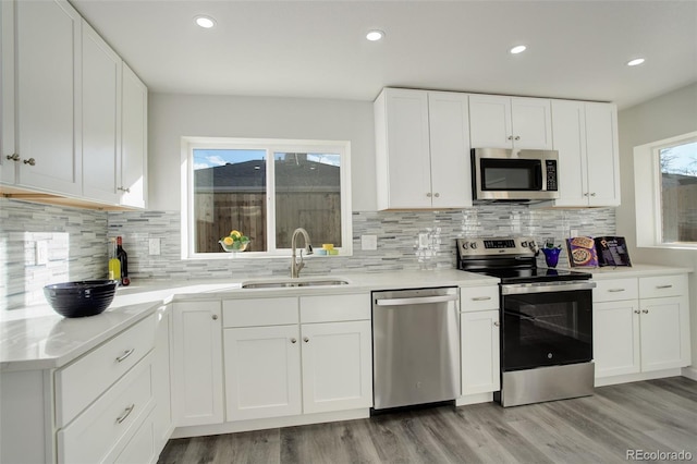 kitchen featuring sink, white cabinetry, stainless steel appliances, tasteful backsplash, and light wood-type flooring