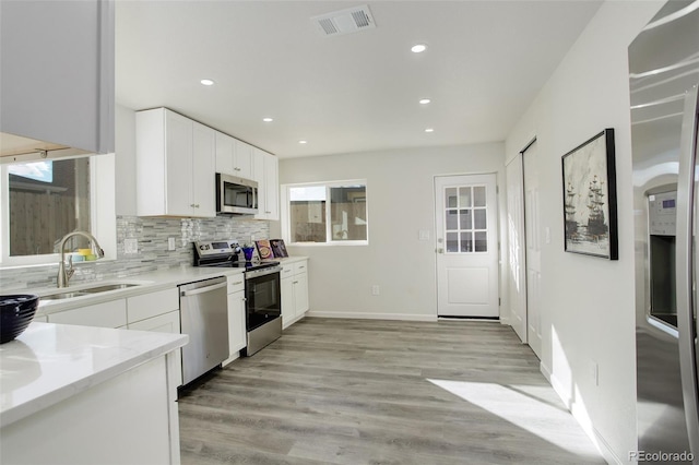 kitchen with appliances with stainless steel finishes, white cabinetry, sink, backsplash, and light hardwood / wood-style floors