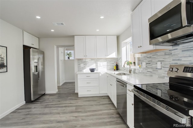 kitchen featuring sink, light hardwood / wood-style flooring, stainless steel appliances, tasteful backsplash, and white cabinets