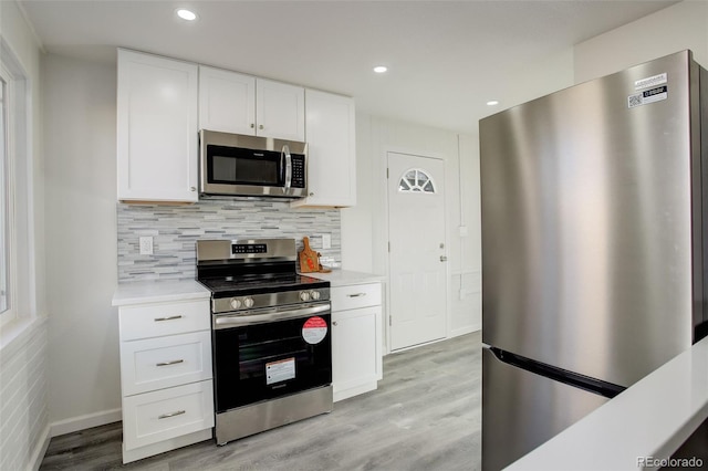 kitchen with stainless steel appliances, decorative backsplash, white cabinets, and light hardwood / wood-style flooring