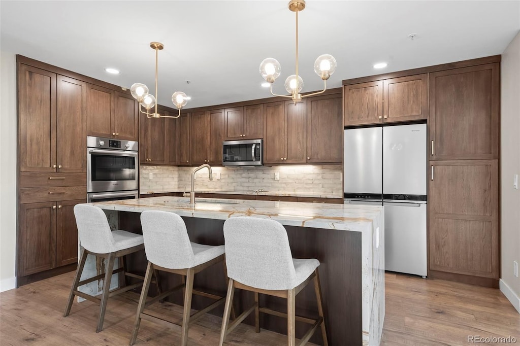 kitchen with decorative light fixtures, a notable chandelier, appliances with stainless steel finishes, and light wood-type flooring