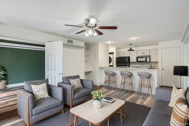 living room with stacked washer / drying machine, visible vents, dark wood-style floors, and ceiling fan