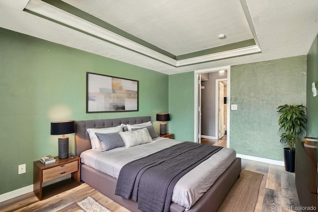 bedroom featuring baseboards, ornamental molding, a raised ceiling, and wood finished floors