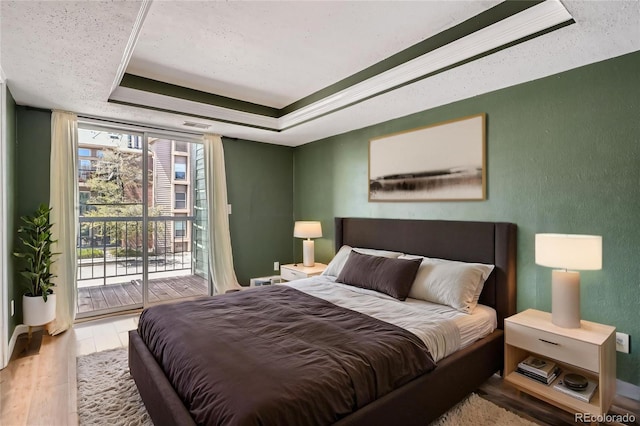 bedroom featuring access to outside, a textured wall, a raised ceiling, wood finished floors, and visible vents