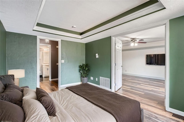 bedroom featuring crown molding, a tray ceiling, wood finished floors, and visible vents