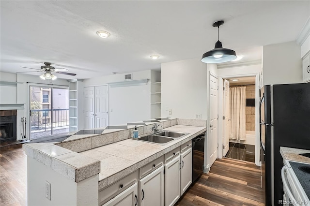 kitchen with ceiling fan, tile countertops, dishwasher, a sink, and a peninsula