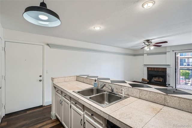 kitchen featuring ceiling fan, a fireplace, a sink, open floor plan, and dark wood-type flooring