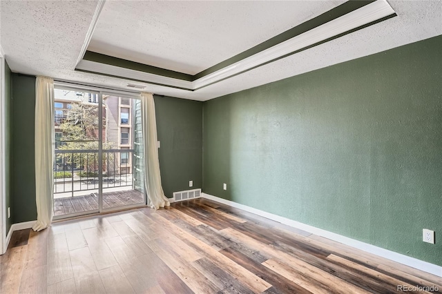 spare room with a textured wall, a tray ceiling, wood finished floors, and visible vents