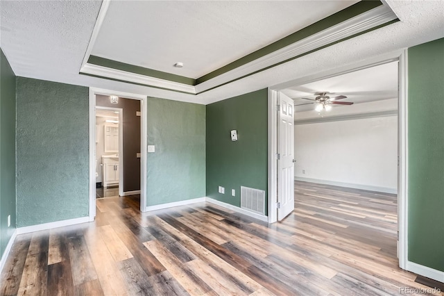 unfurnished room featuring visible vents, a textured wall, wood finished floors, a textured ceiling, and a raised ceiling