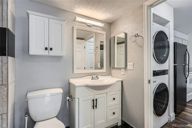 bathroom featuring stacked washer and dryer, a textured wall, vanity, toilet, and a textured ceiling