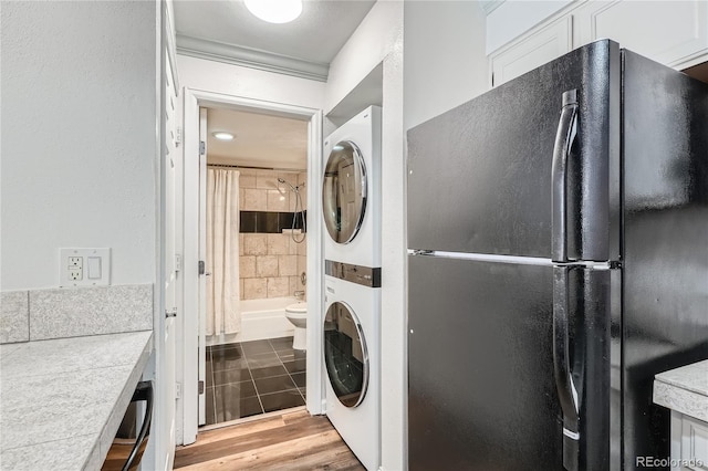 clothes washing area featuring stacked washer / drying machine, wood finished floors, and laundry area