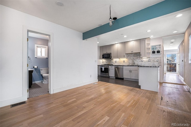 kitchen featuring appliances with stainless steel finishes, hardwood / wood-style floors, sink, dark stone countertops, and backsplash