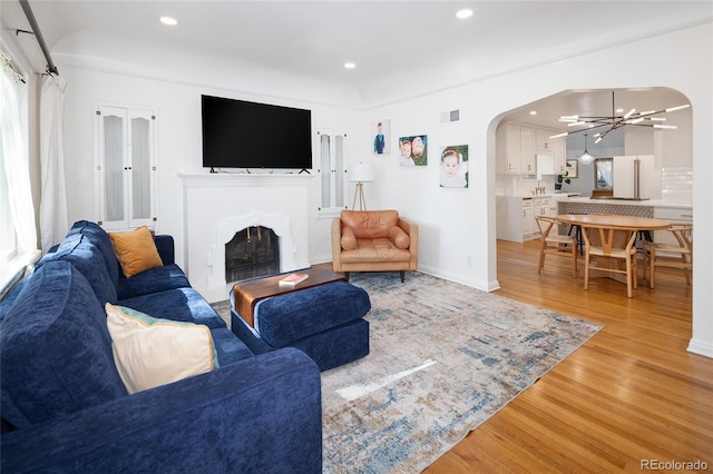 1661 Oneida St, Denver, CO 80220 - living room with arched walkways, light wood-type flooring, a chandelier, a fireplace with flush hearth, and recessed lighting