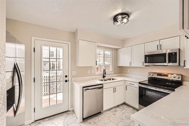 kitchen featuring sink, white cabinetry, light stone counters, a textured ceiling, and appliances with stainless steel finishes