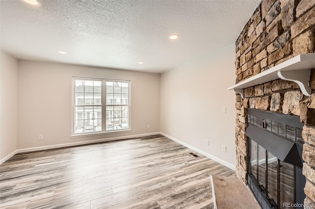 unfurnished living room featuring a stone fireplace, a textured ceiling, and light hardwood / wood-style flooring