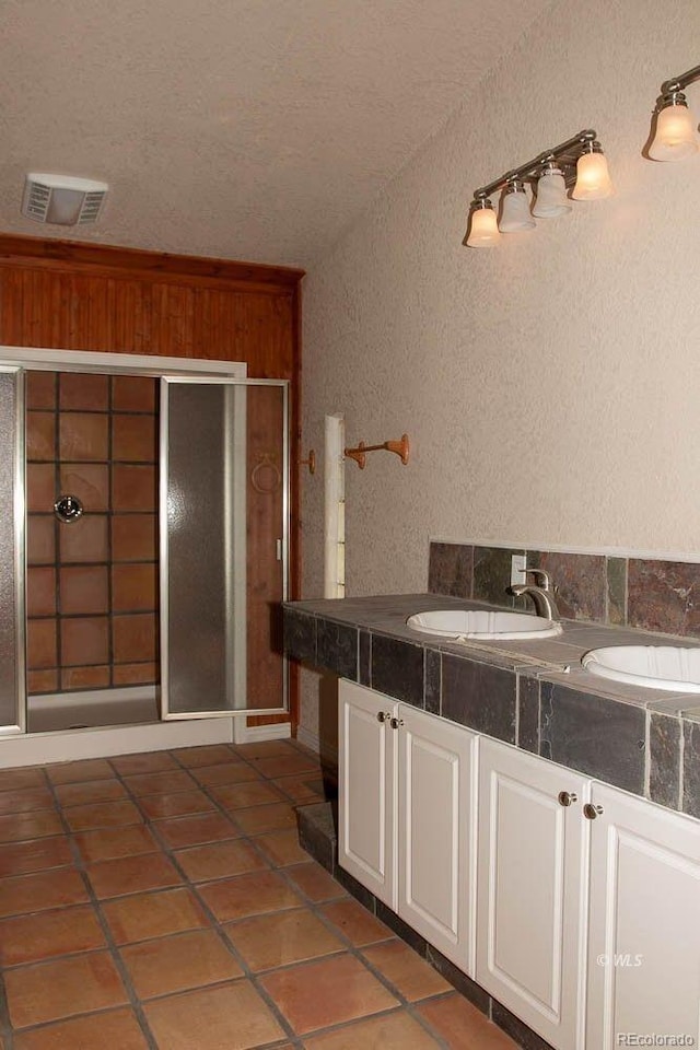 bathroom with a textured ceiling, an enclosed shower, dual vanity, and tile floors