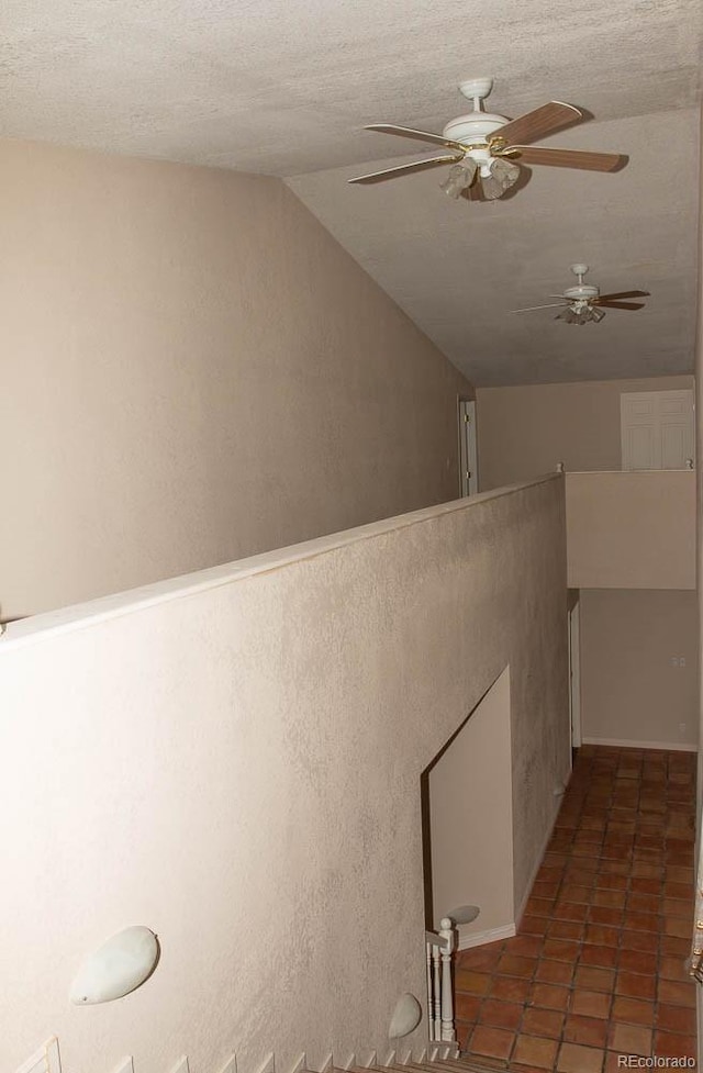 corridor featuring lofted ceiling, dark tile flooring, and a textured ceiling