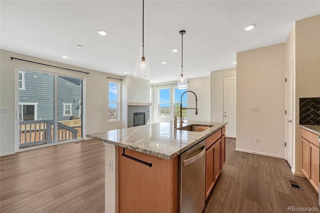 kitchen featuring light hardwood / wood-style flooring, a center island with sink, dishwasher, decorative light fixtures, and sink