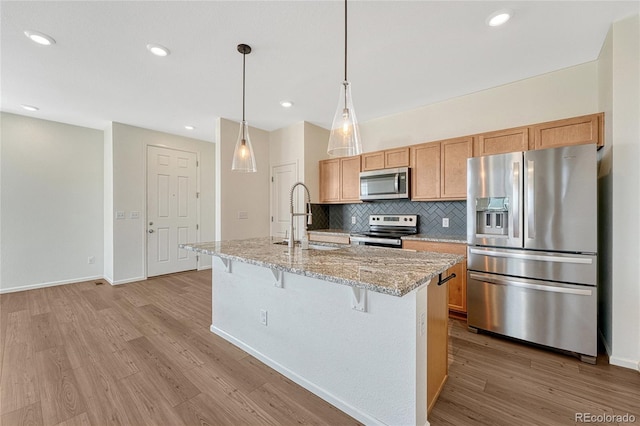 kitchen featuring appliances with stainless steel finishes, light hardwood / wood-style flooring, tasteful backsplash, sink, and an island with sink