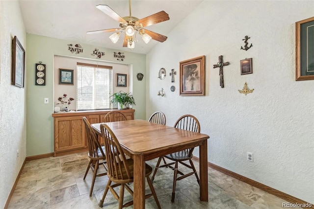 dining room with lofted ceiling, a ceiling fan, stone finish floor, baseboards, and a textured wall