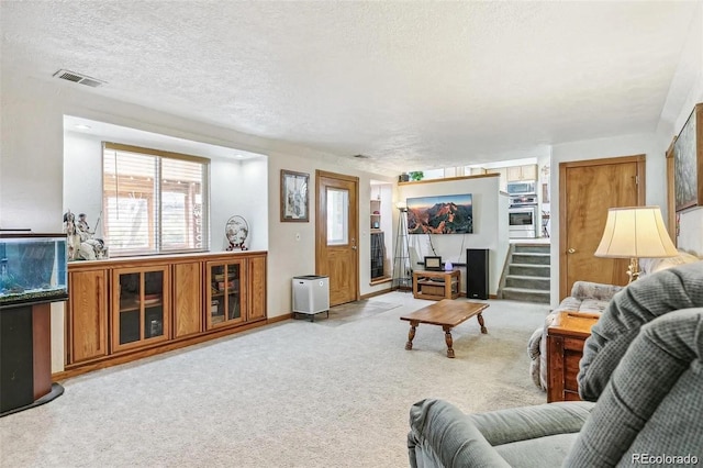 living room featuring a textured ceiling, stairway, visible vents, and light colored carpet